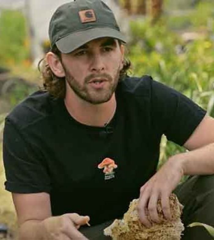 Image of earthed teacher Jack Hodgson, bending over a raised bed of vegetables growing